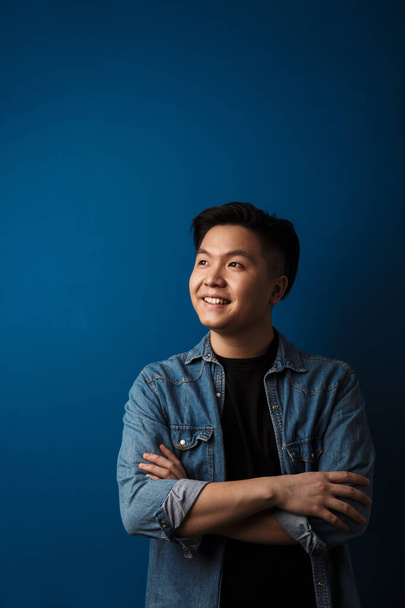 Bild eines zufriedenen gutaussehenden asiatischen Mannes, der vor blauem Hintergrund isoliert nach oben blickt und lächelt - Foto, Bild