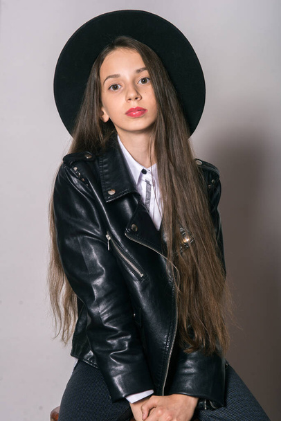 A teenage girl in a trendy leather jacket and an even hat on a white background. Teenage fashion. Street fashion. Beauty and fashion - Zdjęcie, obraz
