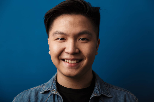 Portrait of a cheerful young asian man wearing casual clothes standing isolated over blue background, looking at camera - Φωτογραφία, εικόνα
