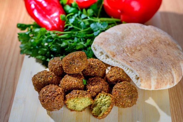 Falafelballen, zoete rode peper, pita-arabisch brood en groene verse peterselie op een rustieke houtachtergrond. Falafel is een traditioneel Midden-Oosten eten, vaak geserveerd in een pitta. - Foto, afbeelding