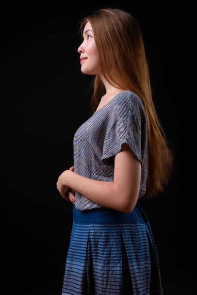 Studio shot of young beautiful woman with long brown hair against black background - Foto, Bild