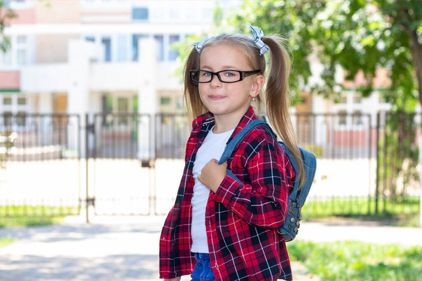 Onnellinen koulutyttö silmälasien kanssa kadulla. valkoinen t-paita ja ruudullinen paita - Valokuva, kuva