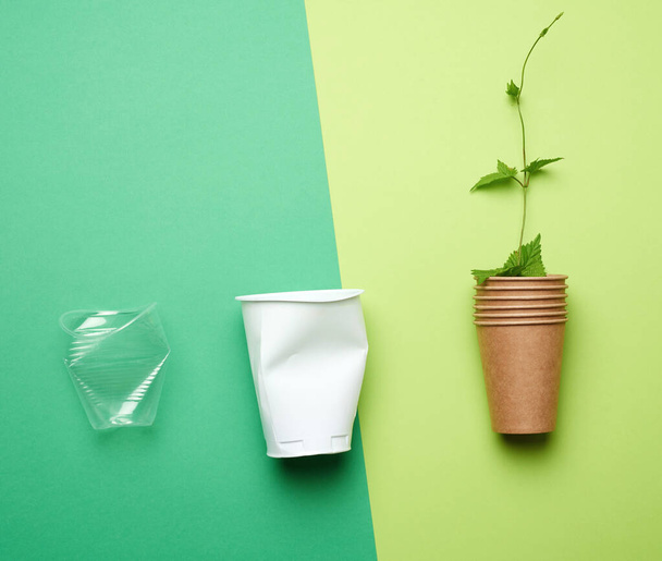 пластикові чашки для напоїв та паперова чашка з гілкою та зеленим листям на зеленому фоні, концепція забруднення навколишнього середовища, без пластику, вид зверху
 - Фото, зображення