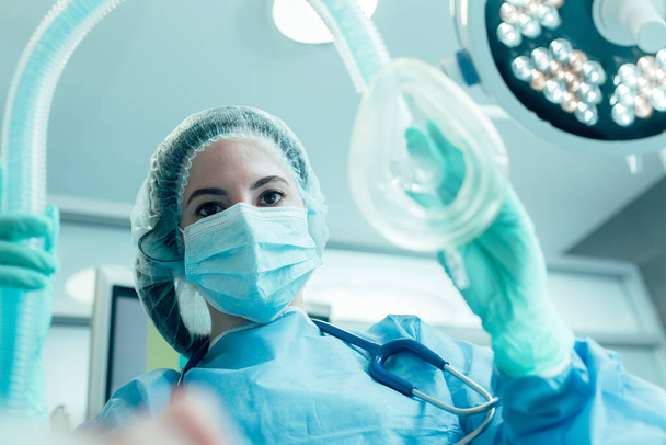 Doctor in medical mask and protective clothes standing with an anesthesia mask in her hand - Foto, Bild