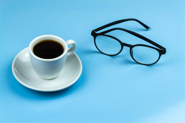 Egy csésze kávé, fekete szemüveg. Kék háttér - Fotó, kép