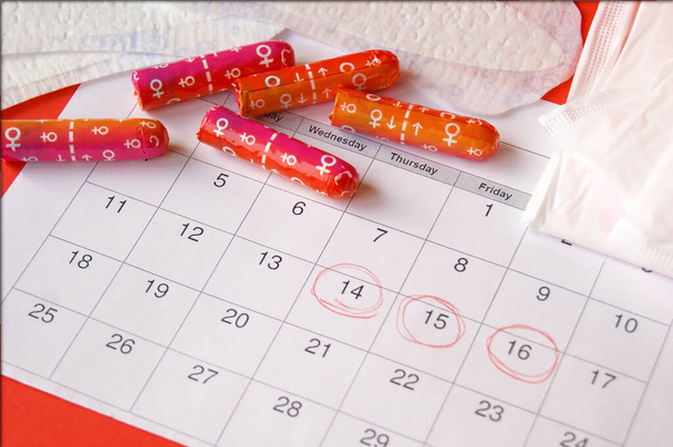 Menstrual pads and tampons on menstruation period calendar with on red background. - Photo, Image