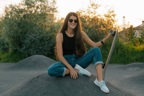 beautiful smiling woman sitting on a hill with skateboard - Foto, imagen