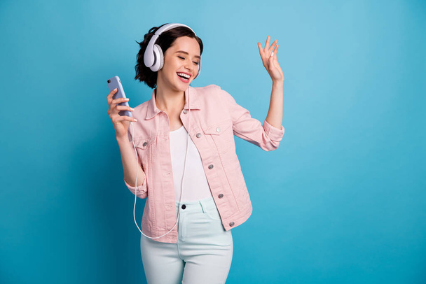 Photo of beautiful cheerful lady hold telephone listen cool modern technology headphones eyes closed enjoy music dancing wear casual pink jacket pants isolated blue color background - Photo, image