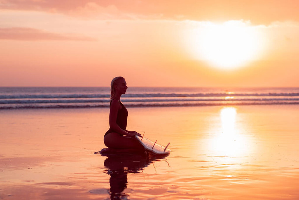 Portrait of surfer girl with beautiful body on the beach with surfboard at colourful sunset time in Bali - Фото, зображення