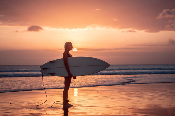 Portrait of surfer girl with beautiful body on the beach with surfboard at colourful sunset time in Bali - Фото, изображение