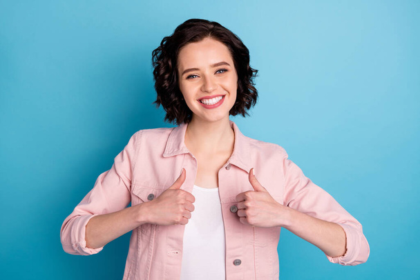 Photo of attractive cheerful lady short black hairdo raise thumb fingers up expressing positive attitude agreement wear casual pink denim jacket isolated blue color background - Fotoğraf, Görsel