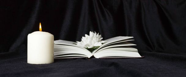 Tarjeta de condolencias. Una vela conmemorativa blanca con flores blancas y un libro abierto. El funeral, la tristeza. - Foto, imagen