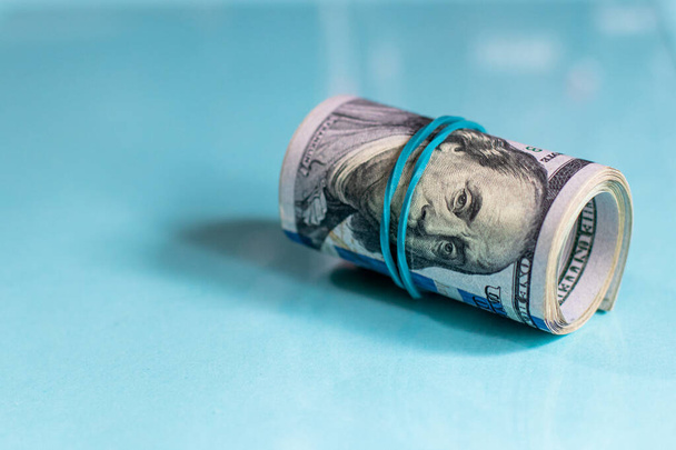 US dollars rolled up and tightened with colored band on light blue background - Photo, Image
