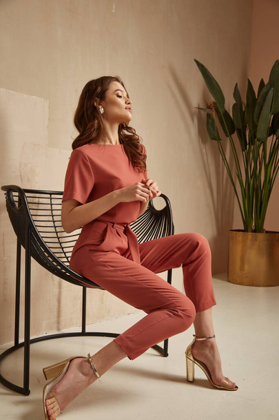 Beautiful brunette woman natural makeup wear fashion clothes casual dress code office style total pink blouse and pants suit, romantic date business meeting accessory armchair interior stairs flowerpot. - 写真・画像