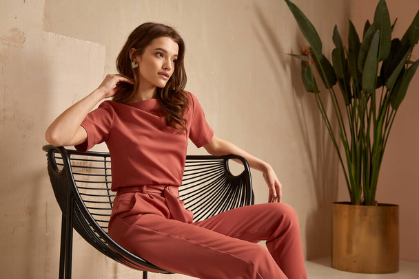 Beautiful brunette woman natural makeup wear fashion clothes casual dress code office style total pink blouse and pants suit, romantic date business meeting accessory armchair interior stairs flowerpot. - Fotografie, Obrázek