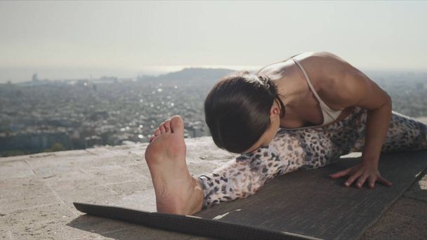Girl performing yoga at viewpoint of Barcelona. Yoga trainer stretching body - Photo, Image