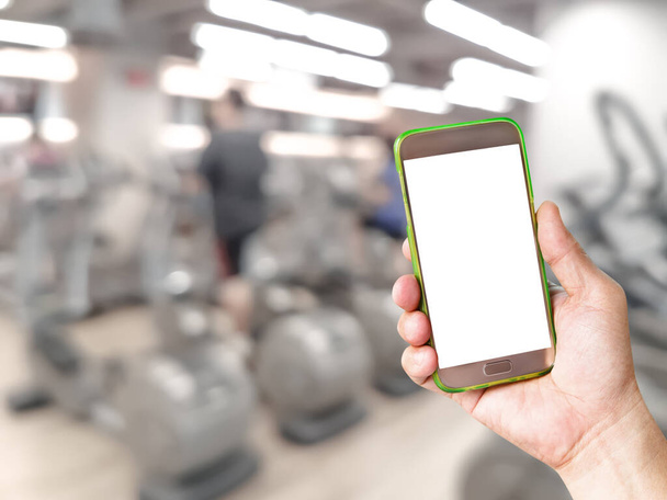 mão segurando telefone inteligente móvel com fundo de equipamento de ginásio de fitness desfocado
 - Foto, Imagem