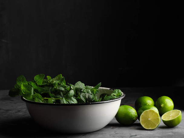 In a rustic white cup is a peppermint cut lime on the right against a dark background. Mojito ingredients. - Foto, afbeelding