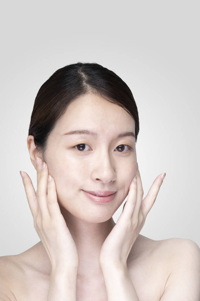 Asiatische junge Frau berührt Gesicht mit ihrer Hand in entspanntem Ausdruck - Foto, Bild