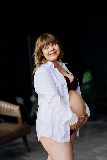 raskaana oleva nainen, jolla on ylipaino alusvaatteissa seisoo ja silitti vatsa. - Valokuva, kuva