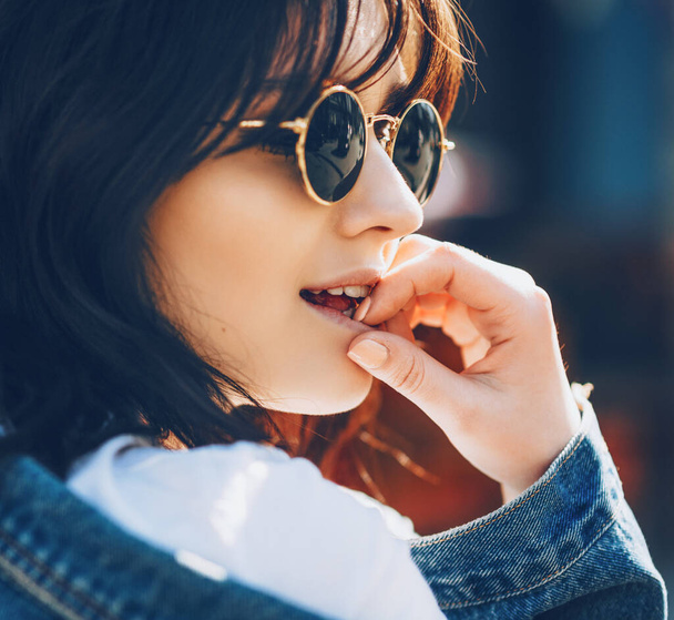 Close up photo of a fashionable caucasian brunette woman with eyeglasses touching her lips outside - Foto, Imagem