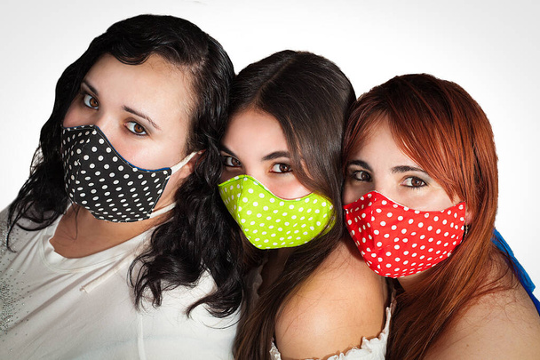 drei Freundinnen mit bunter Gesichtsmaske schützen sich vor Covid Coronavirus 19 isoliert auf weißem Hintergrund - Foto, Bild