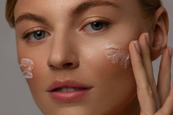 Closeup happy young woman applying cream to her face Skin care and cosmetics concept. Cosmetics. Woman face skin care.Natural makeup, touching face. - Photo, image