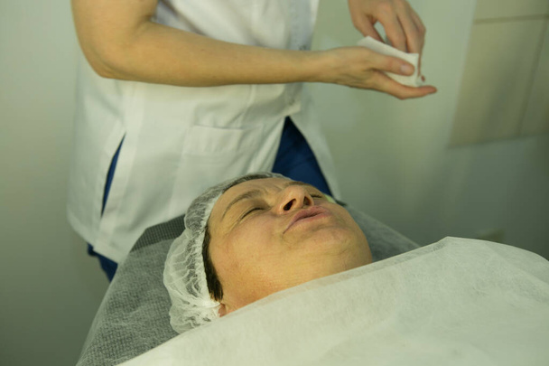 Ein Besuch bei der Kosmetikerin. Verfahren-Carboxytherapie. Der Arzt entfernt die Verjüngungsmaske aus dem Gesicht des Patienten. - Foto, Bild