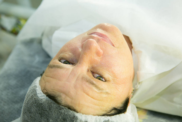 Una visita al esteticista. Procedimiento-carboxiterapia. El médico retira la máscara rejuvenecedora de la cara del paciente. - Foto, imagen