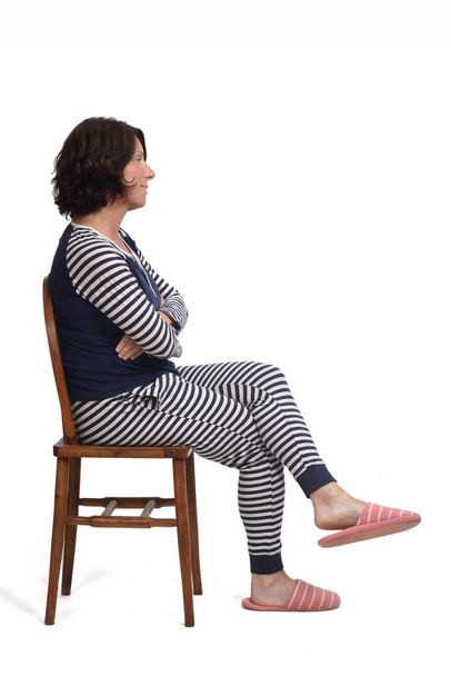 вид збоку жінки в піжамі, що сидить на стільці на білому фоні, схрещені руки і ноги
, - Фото, зображення