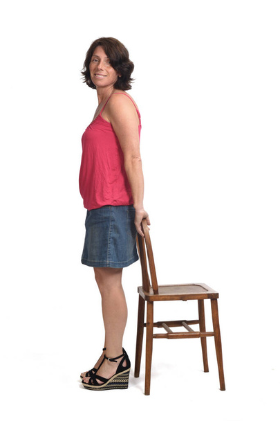  γυναίκα σε denim φούστα παίζει με μια καρέκλα σε λευκό φόντο,  - Φωτογραφία, εικόνα
