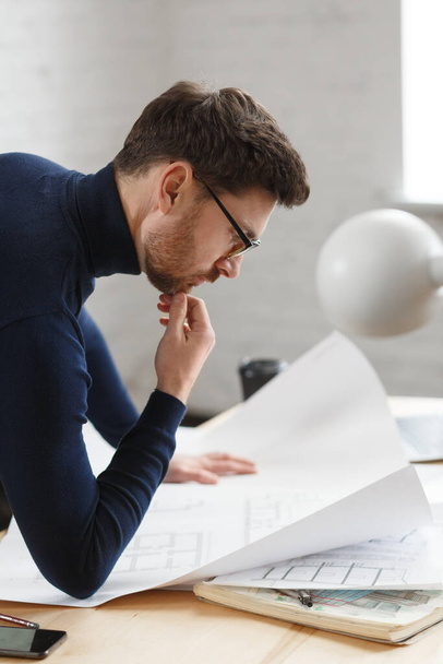 Architect working in office with blueprints.Engineer inspect architectural plan, sketching a construction project.Portrait of handsome bearded man sitting at workplace. Business construction concept - Φωτογραφία, εικόνα