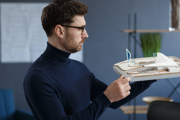 Architect working in office with building 3D model. Engineer inspect building layout, searching new ideas for construction project. Handsome bearded man at workplace. Business construction concept - Photo, image