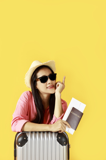 Ázsiai nők hosszú haj visel szalma kalap, napszemüveg a kezében útlevél könyv és utazási táska fénymásoló hely banner. Fiatal lány kész utazni bőrönddel és útlevéllel sárga alapon. Nyár - Fotó, kép