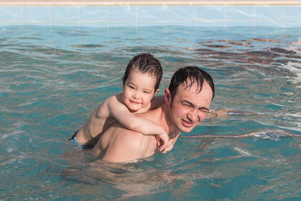 Szczęśliwy ojciec i syn spędzają razem czas pływając w basenie termalnym. - Zdjęcie, obraz