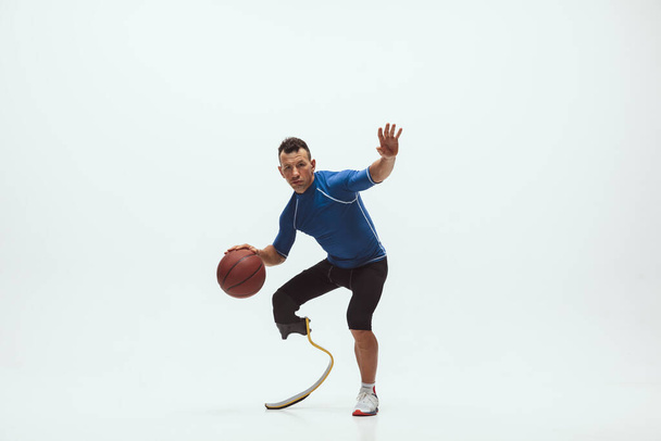 Athlete with disabilities or amputee isolated on white studio background. Professional male basketball player with leg prosthesis training and practicing in studio. - Foto, immagini
