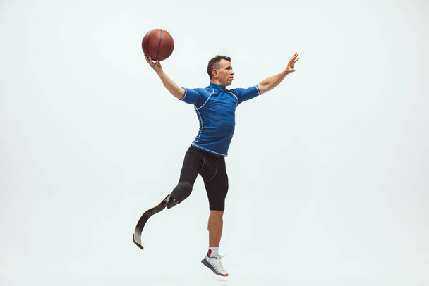 Athlete with disabilities or amputee isolated on white studio background. Professional male basketball player with leg prosthesis training and practicing in studio. - Foto, Bild