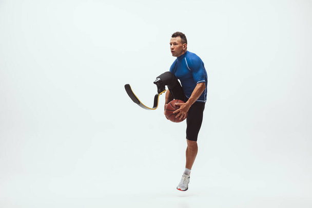 Athlete with disabilities or amputee isolated on white studio background. Professional male basketball player with leg prosthesis training and practicing in studio. - Фото, зображення