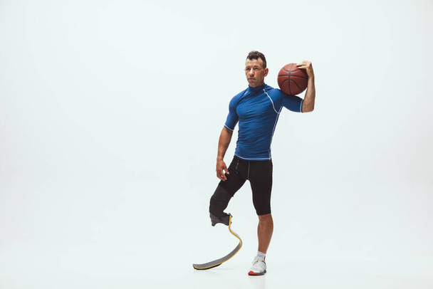 Athlete with disabilities or amputee isolated on white studio background. Professional male basketball player with leg prosthesis training and practicing in studio. - Φωτογραφία, εικόνα