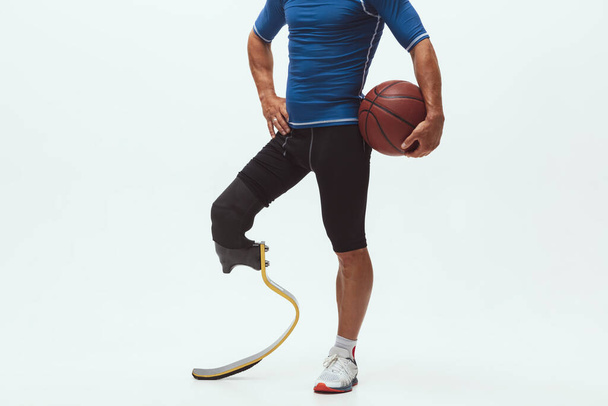 Athlete with disabilities or amputee isolated on white studio background. Professional male basketball player with leg prosthesis training and practicing in studio. - Photo, Image