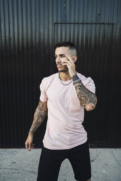 A vertical shot of a young hip tattooed male standing in front of a garage - Photo, image