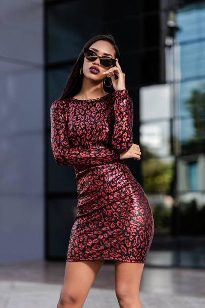 A young African-American woman in an elegant red dress posing in front of a modern office building - Foto, Imagem