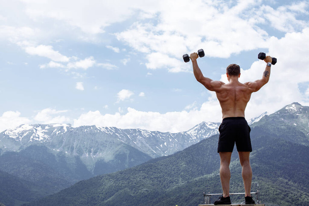 Muscular male athlete with arms raised doing lifting exercises dumbbells. - Φωτογραφία, εικόνα