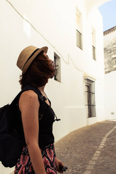 Attraktive junge Frau besucht eine Altstadt, während sie während der Coronavirus-Pandemie eine Gesichtsmaske trägt - Foto, Bild