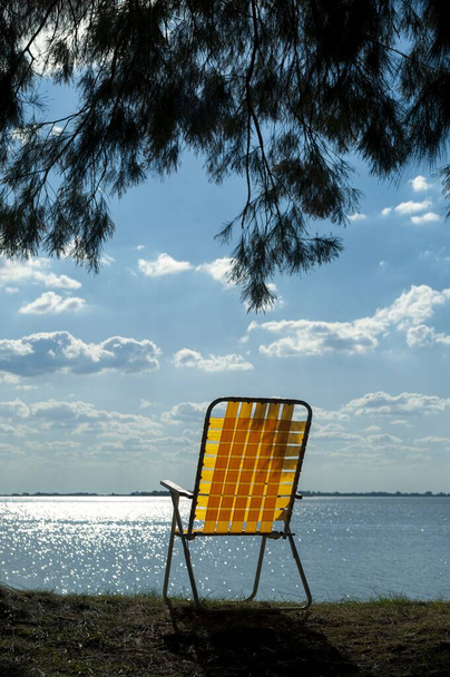 A yellow beach chair placed on the shore of a tranquil lake - Fotó, kép