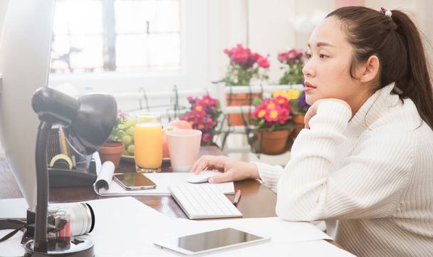 自宅で働く若い女性は、美しい花で飾られた部屋の机の上にコンピュータ、携帯電話やノートパソコンを使用して、部屋で働くことに満足して、自宅のオフィスからのビジネスです。 - 写真・画像
