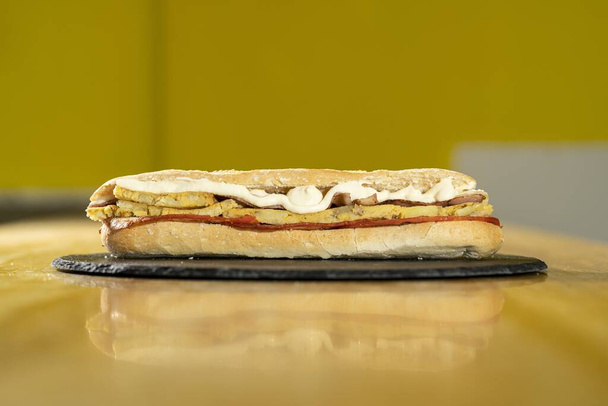 Gros plan d'un sandwich à la mayonnaise sur une planche ronde noire sur une table en bois - Photo, image