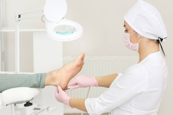 Peeling feet with special electric device.Professional hardware pedicure using electric machine.Patient on medical pedicure procedure, visiting podiatrist.Foot treatment in SPA salon.Podiatry clinic - Фото, изображение