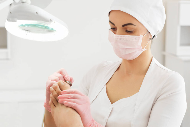 Peeling feet with special electric device.Professional hardware pedicure using electric machine.Patient on medical pedicure procedure, visiting podiatrist.Foot treatment in SPA salon.Podiatry clinic - Фото, зображення