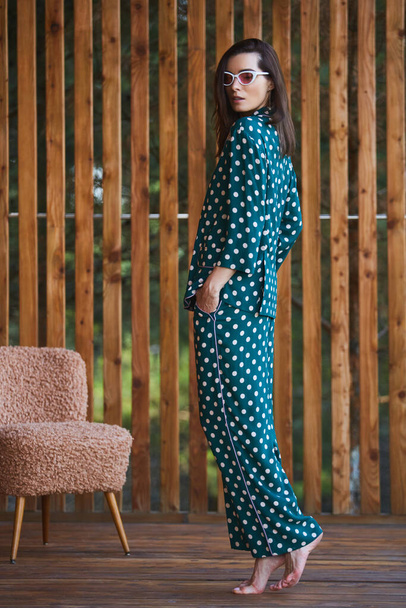 Woman standing in pajamas pajamas with polka dots on wooden background in full length. Caucasian female model. - Photo, image